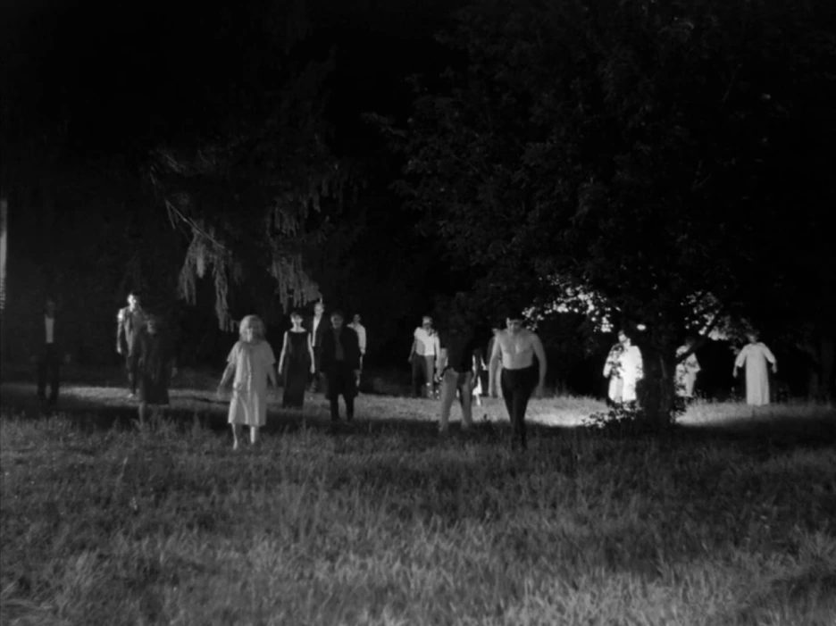 A crowd of the walking dead advancing across a dark field in a black-and-white still